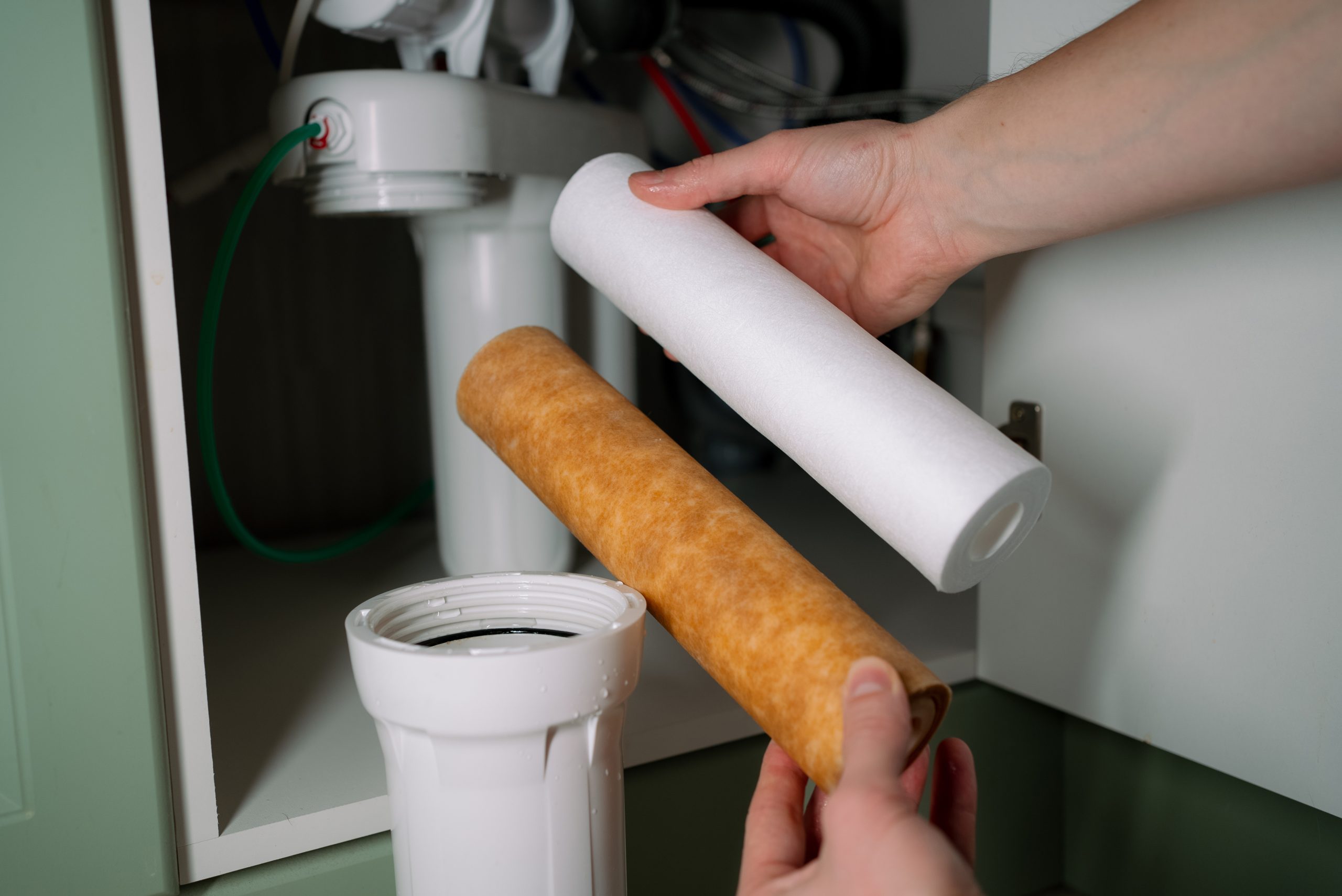 Person's hands replacing a dirty water filter cartridge with a new clean one, improving home drinking water purification for health and sanitation